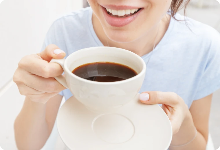 Femme buvant du café, aliment à éviter après un blanchiment dentaire