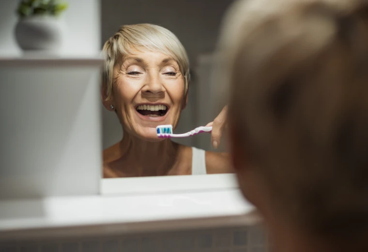 Patiente se brossant les dents devant un miroir dans le cadre de l'entretien d'une prothèse sur implants